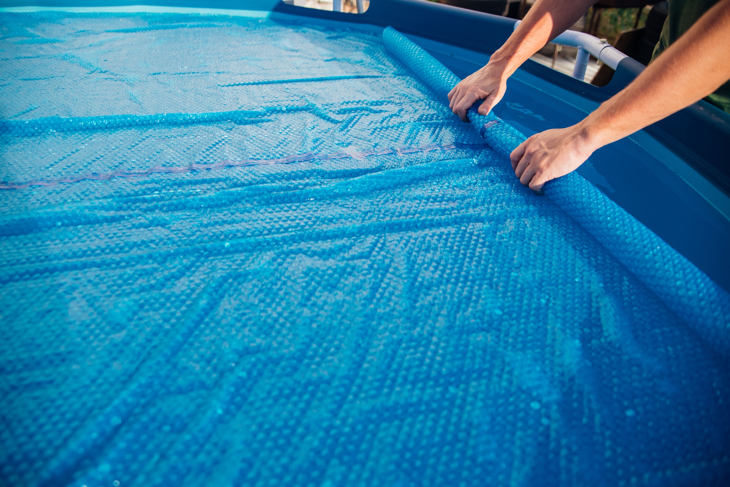 Lona para piscina azul sendo colocada sobre a água para proteção, ajudando a manter a piscina limpa e reduzir sujeira externa.